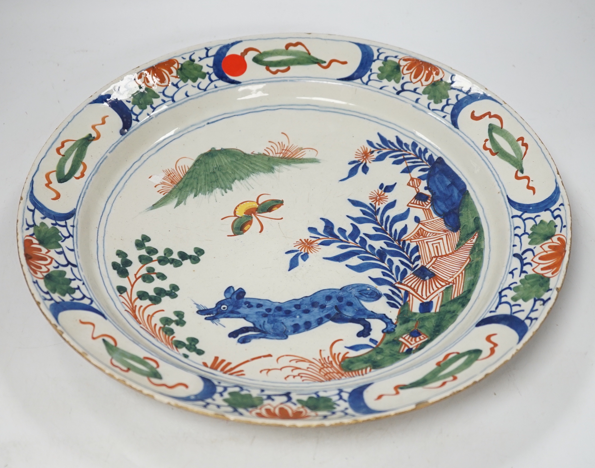 An 18th century delftware dish, the centre painted with a wolf, a bee and a pavilion, 35cm